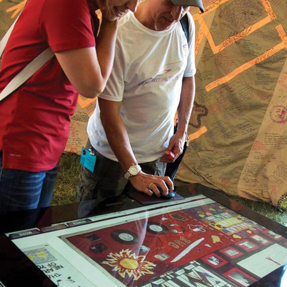 Color photo of two individuals staring down at what looks to be a sort of digital gaming table.