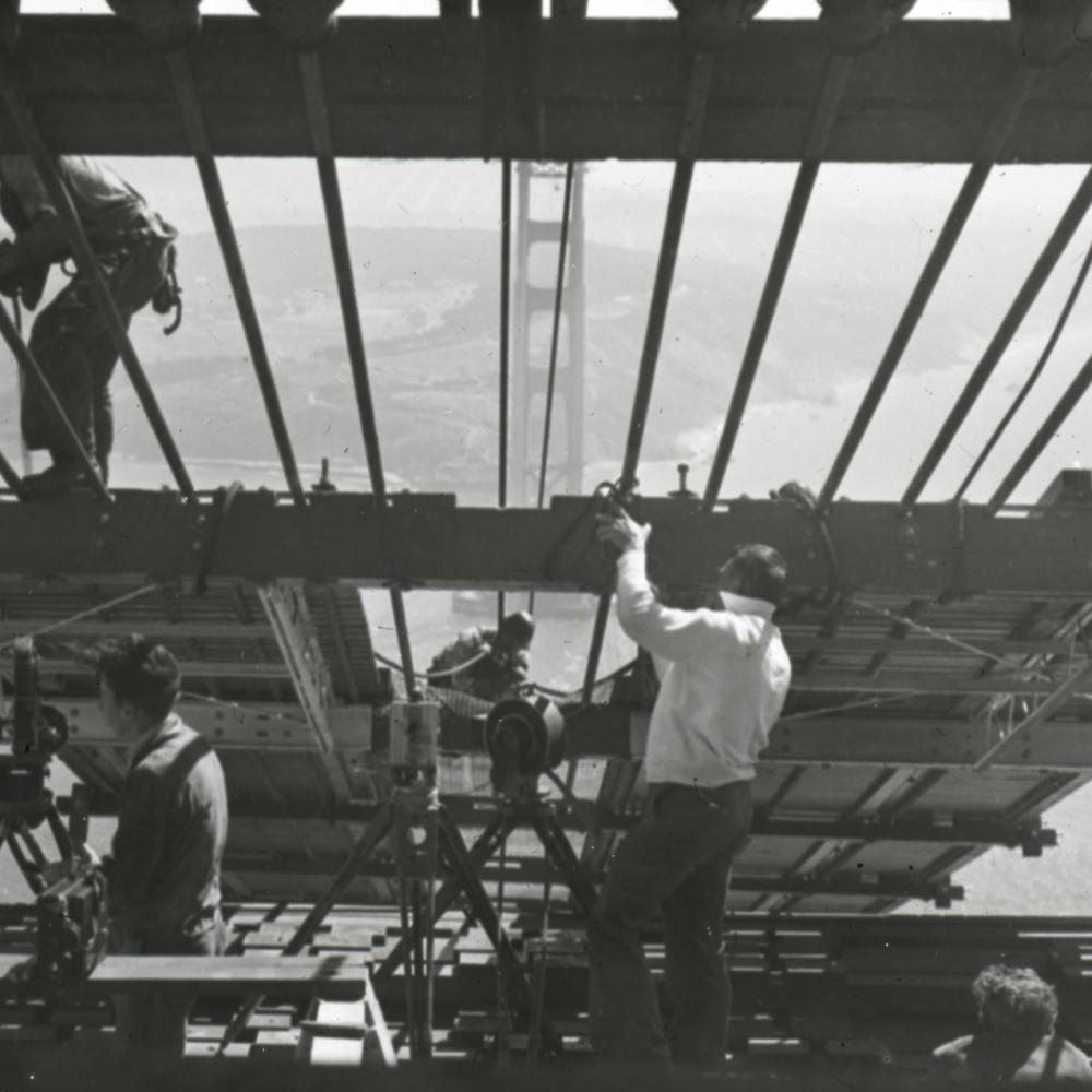 Black and white photo of men working on the Golden Gate bridge, high up in the air.