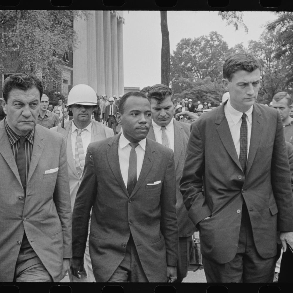 Black and white photo of bureaucrats in suits walking as an entourage.