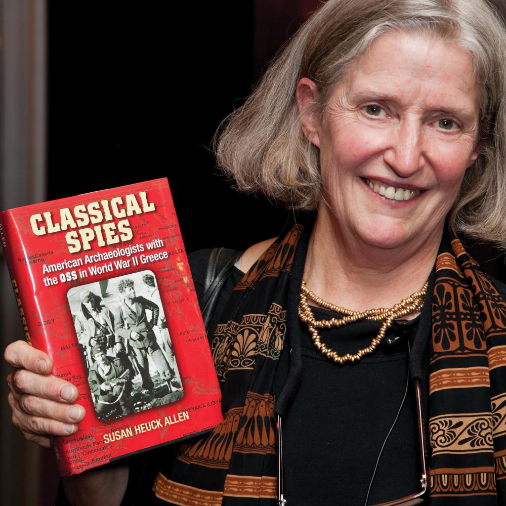 Heuck Allen in a striped scarf, posing with her book "Classical Spies"