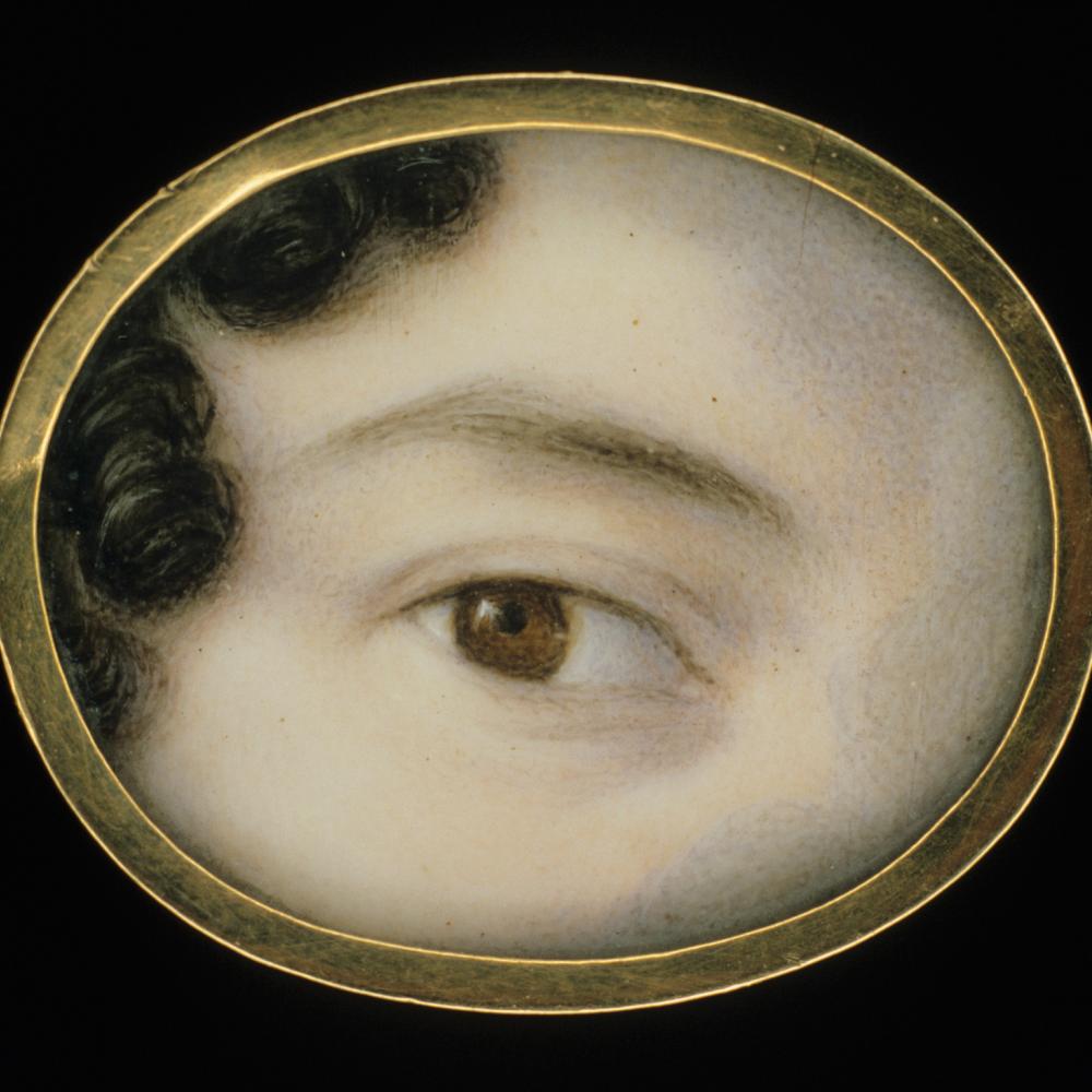 close up of a woman's brown eye, framed by a thin dark eyebrow and pale skin