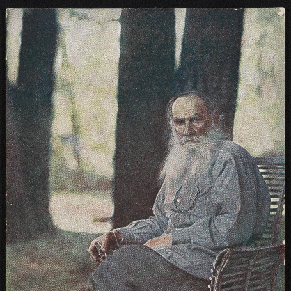 Tolstoy in a blue shirt and boots, long white beard, sitting under trees on a wood bench
