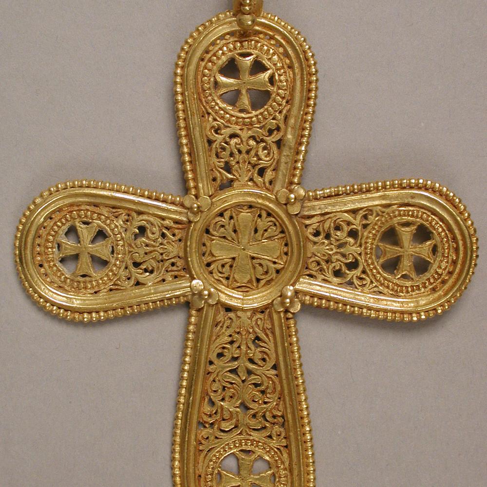 A gold pendant in the shape of a cross, with rounded edges and intricate filigree designs