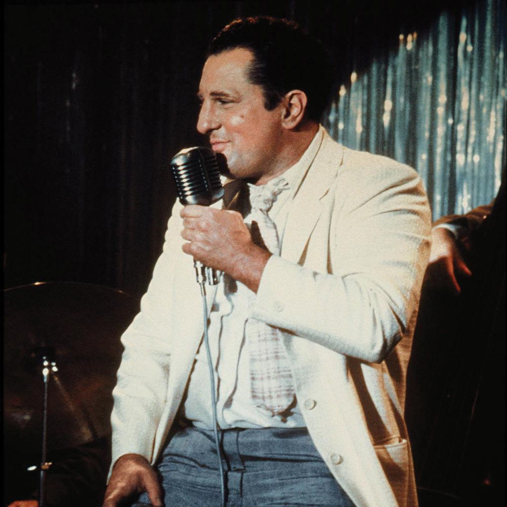 De Niro singing onstage in a white suit jacket, in a scene from Raging Bull