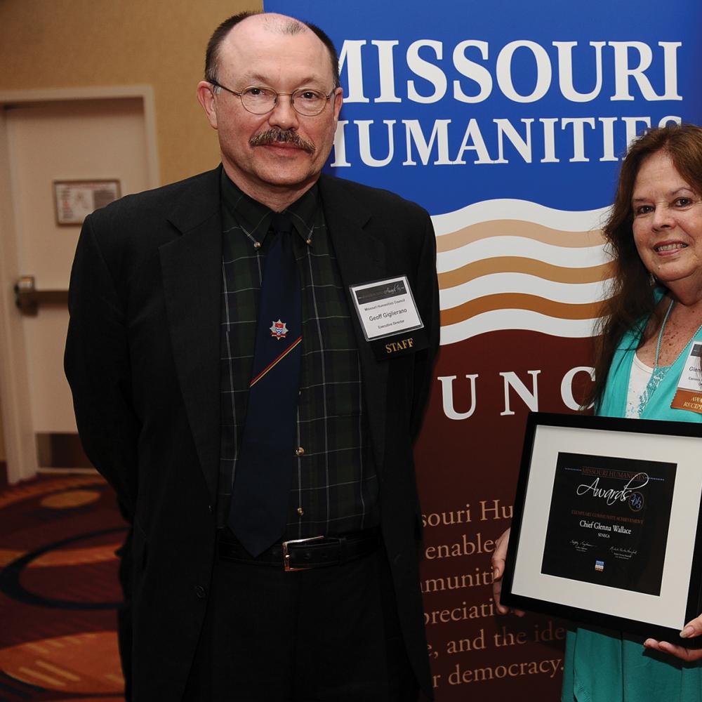 Giglierano and Wallace, posing with Wallace's award in front of a Missouri Humanities poster