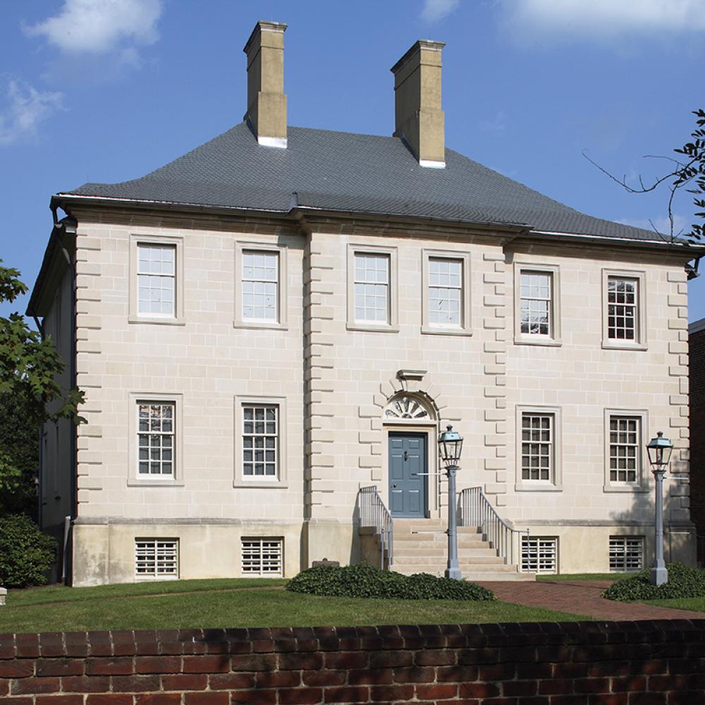 White house with French windows, gray roof, and two chimneys, with a small green lawn surrounding