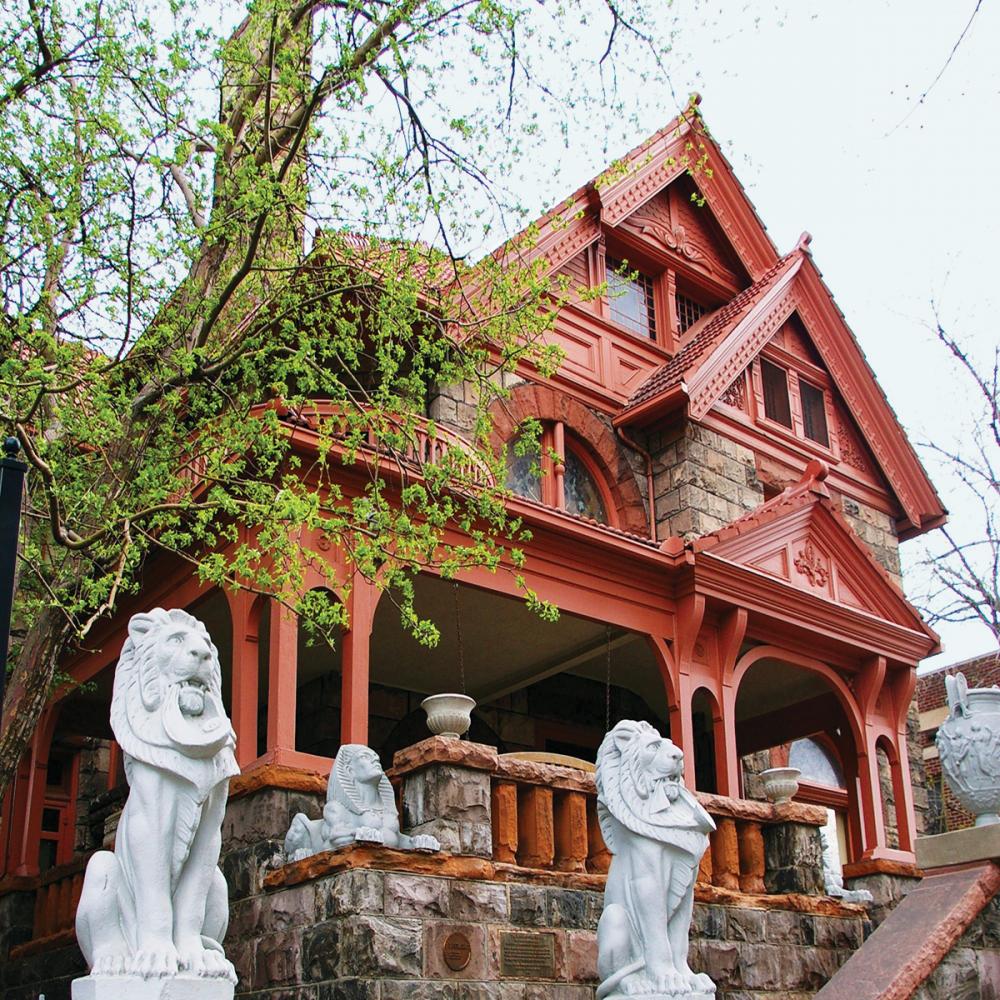 Color photo of an ornate, wide-brick home with red painted trim and columns. 