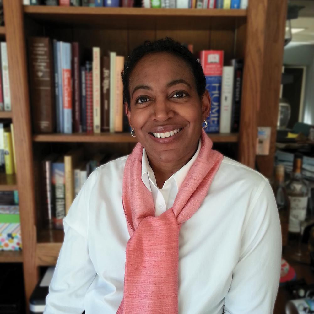 Color photo of Brenda Thomson sitting in front of a library, wearing a red scarf.