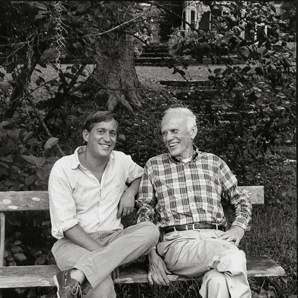 Black and white photo of Walter Isaacson and Walker Percy sitting on a bench, smiling.