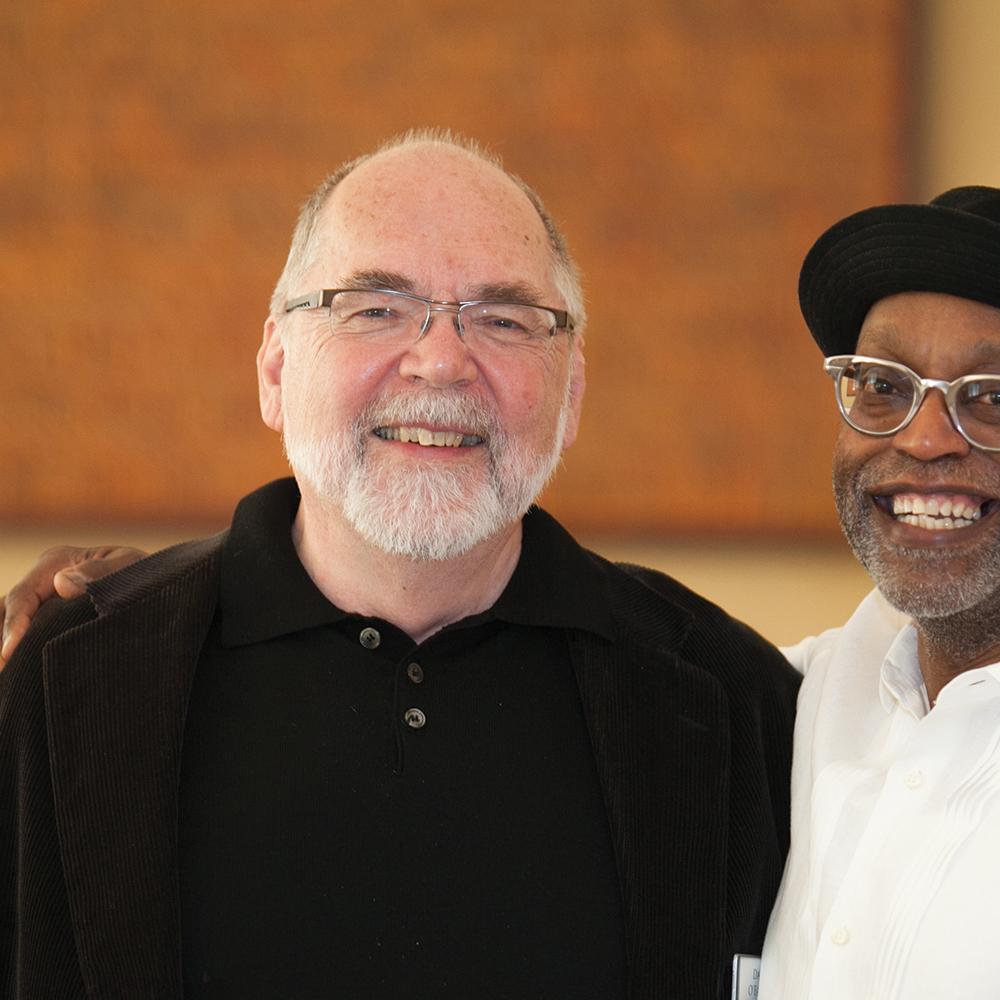 O'Fallon, black turtleneck and glasses, and Jones, wearing a black hat and glasses