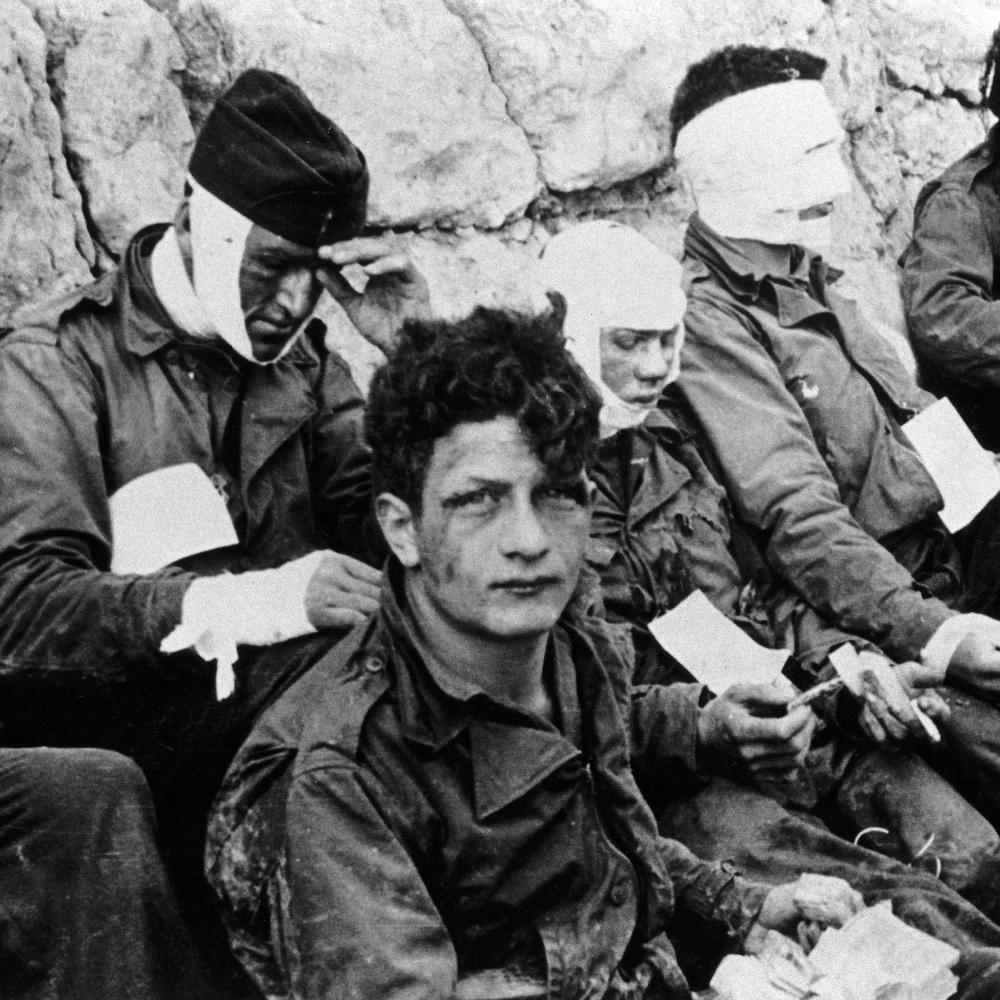 Four american soldiers, three with heavy bandaging over their faces, sitting and waiting