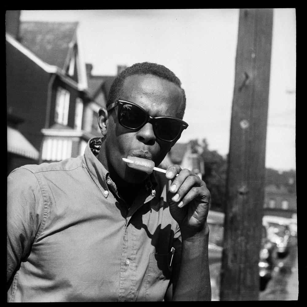 A young, African American man wearing sunglasses and eating a popsicle