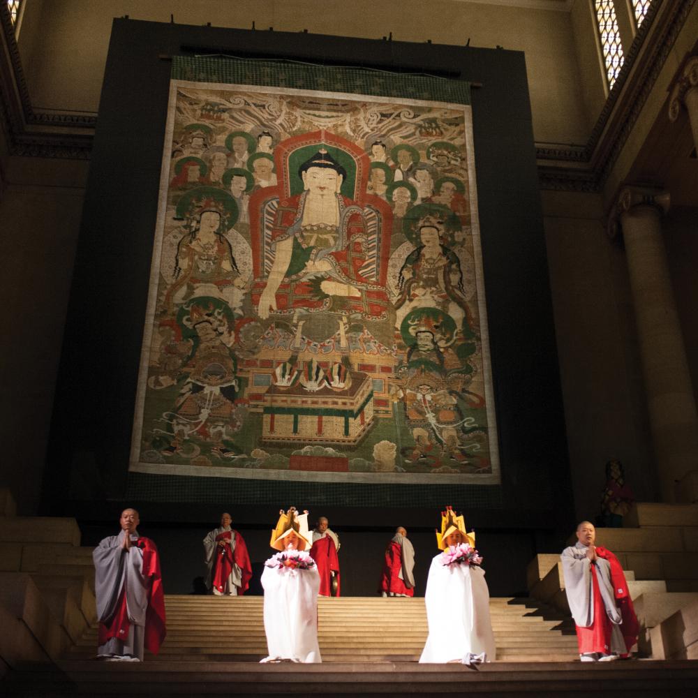 The Śākyamuni Assembly, hanging on a stage, with monks performing in front of it