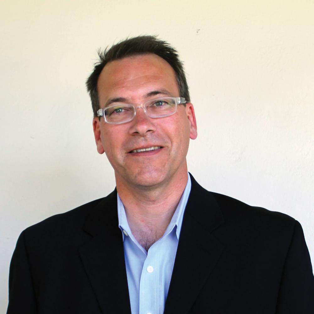 Color photo of David Igler wearing a blue collared shirt and black blazer.