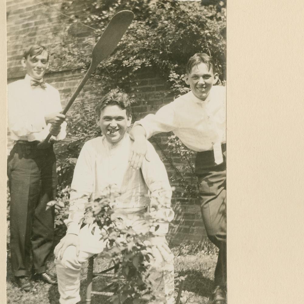 An old photograph of the Mencken brothers in their backyard. One of them is holding an oar over H.L. Mencken's head.