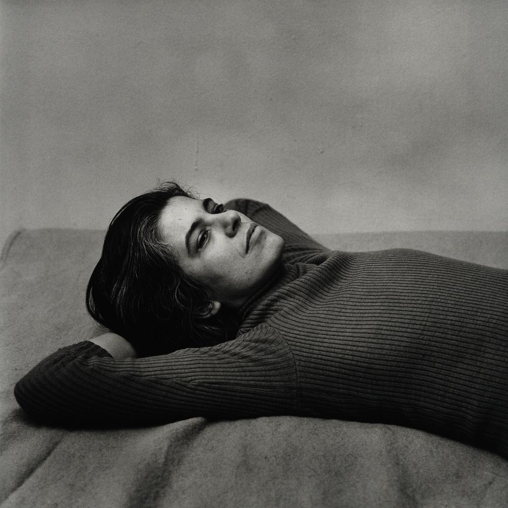 black and white photo of Sontag, lying down with her hands underneath her head