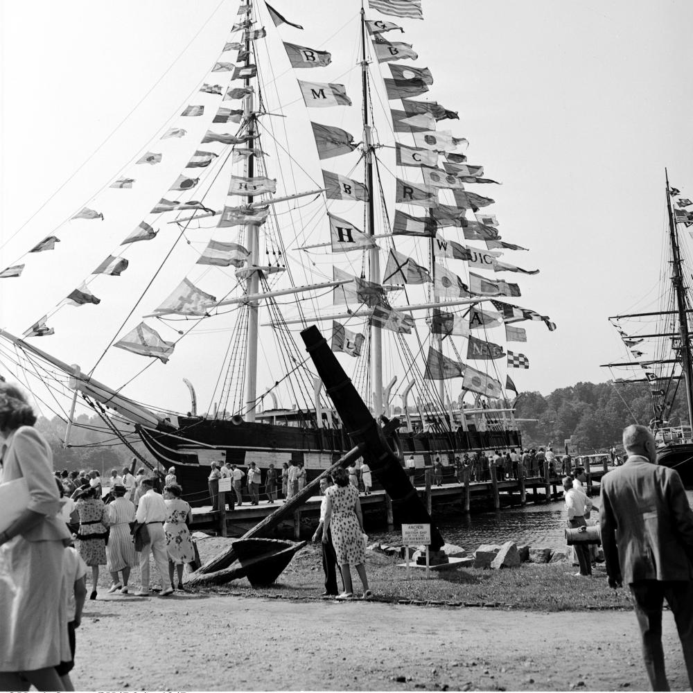 black and white photo of the Charles W Morgan ship, surrounded by people with flags fluttering