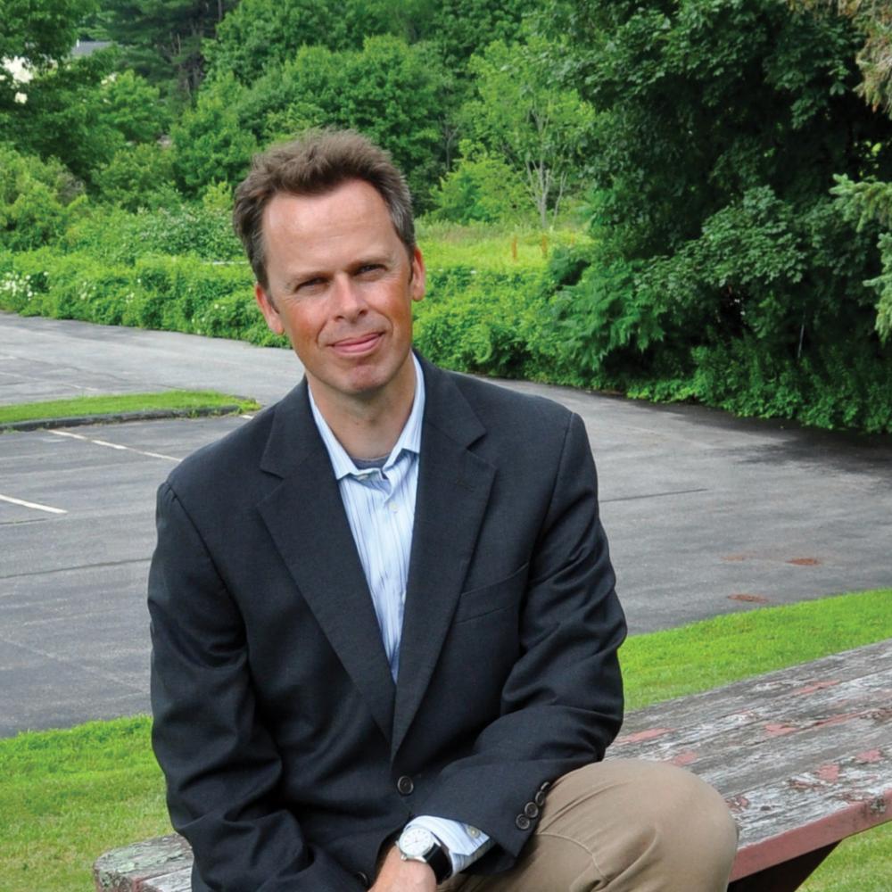 Professional photo of Hayden Andersen sitting at a picnic table with trees in the background.