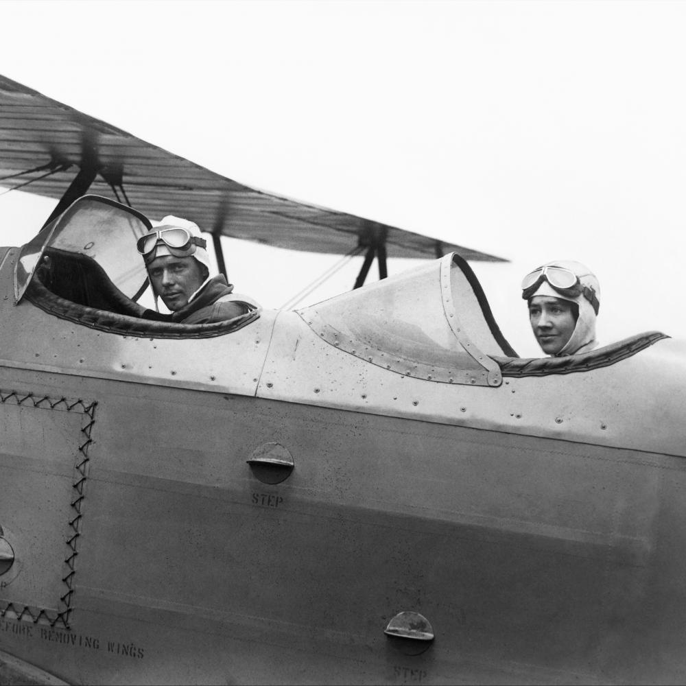 Black and white photo of two individuals sitting in their respective cockpit seats in a plane.
