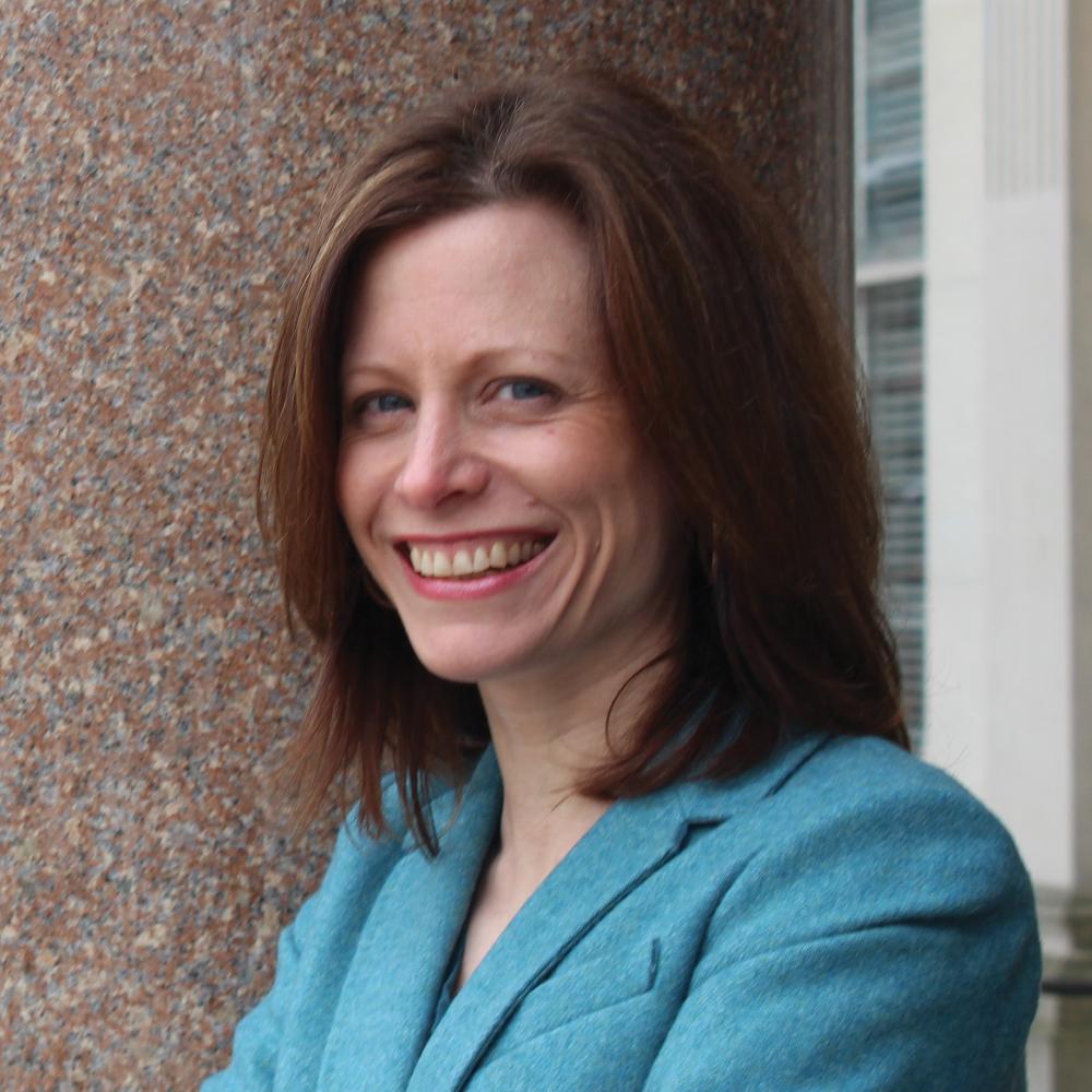 Briann Greenfield, wearing an aqua blue blazer, standing with her arms folded, smiling
