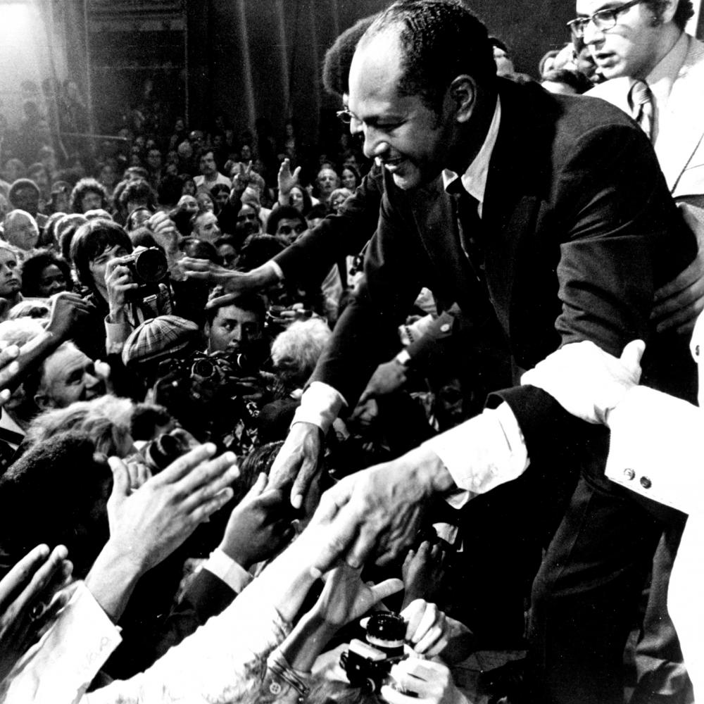 Mayor-elect Tom Bradley shaking hands with a crowd of people, reaching out their hands to him