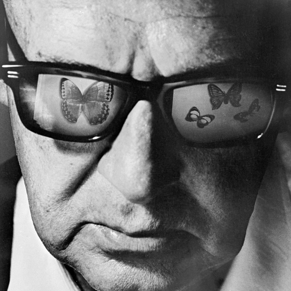 black and white close-up portrait of a man wearing glasses, which reflect butterflies