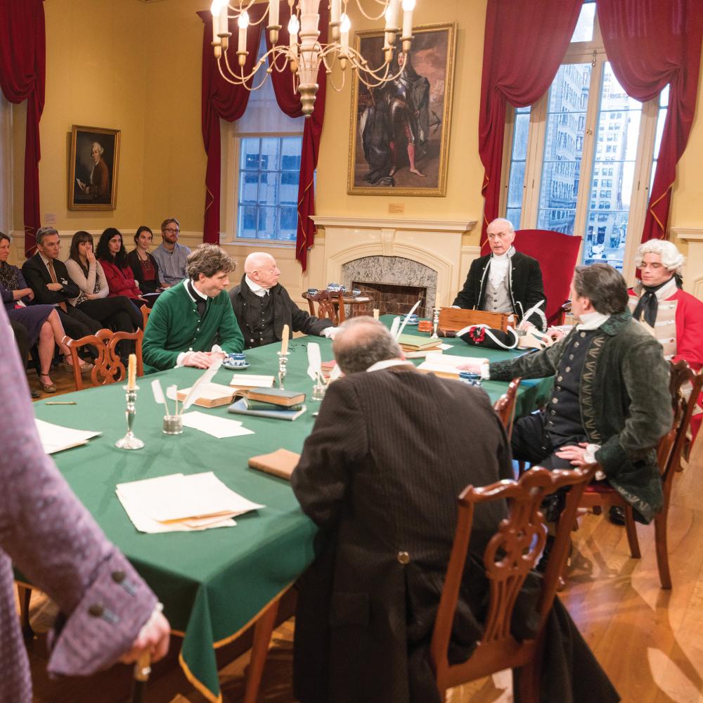 Photograph of men in period clothing and wigs at a table