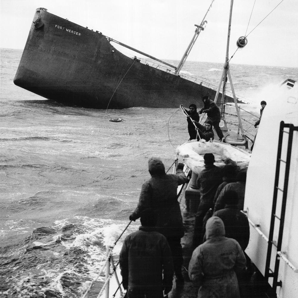 Black and white photo of men pulling in a life raft from a sinking ship.