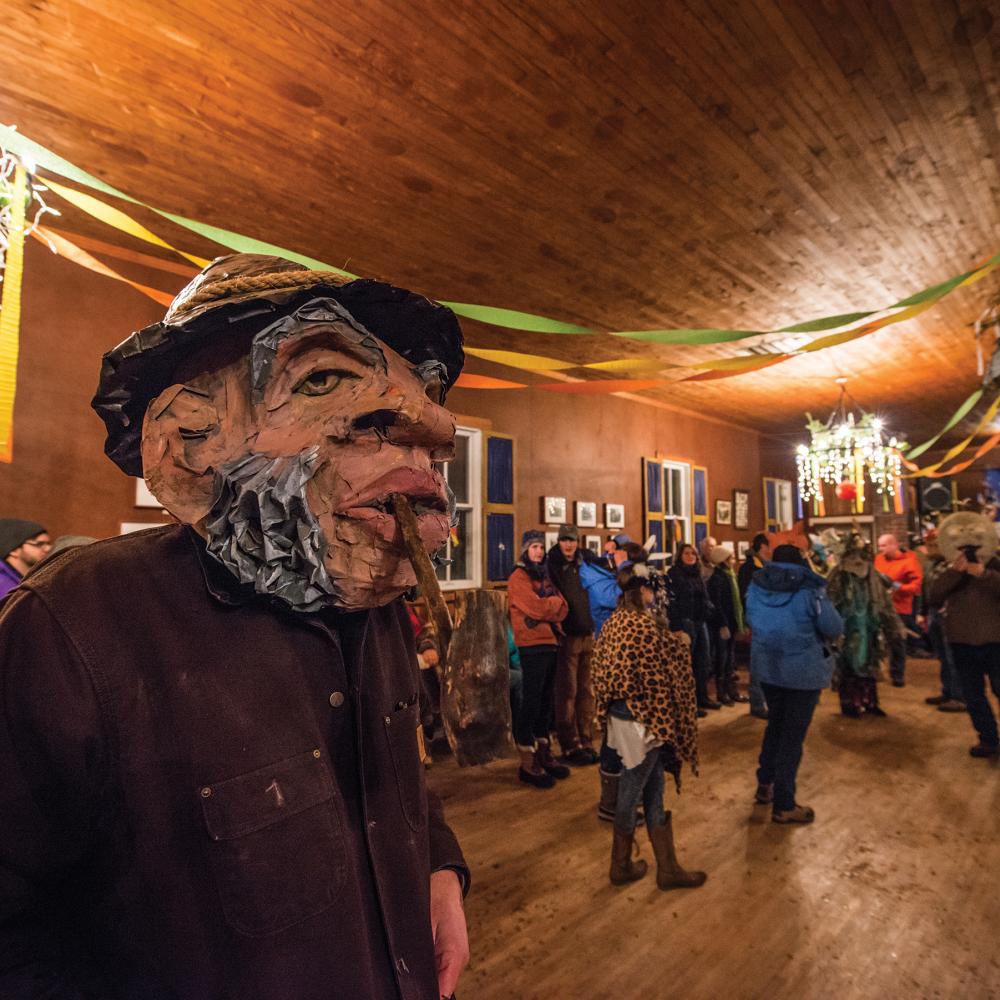 Color photo of a man wearing a mask at a costume festival, indoors.