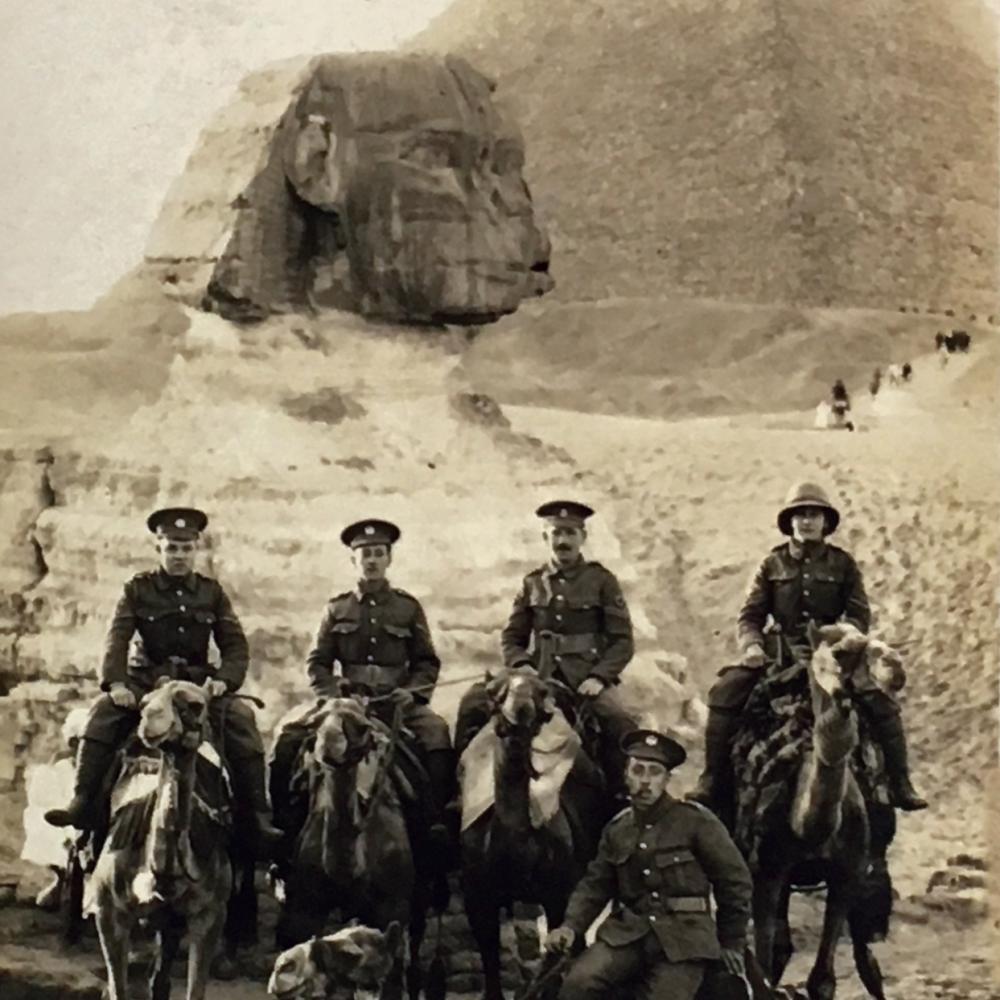 Sepia-colored photo of mounted soldiers posing before the pyramids of Egypt.