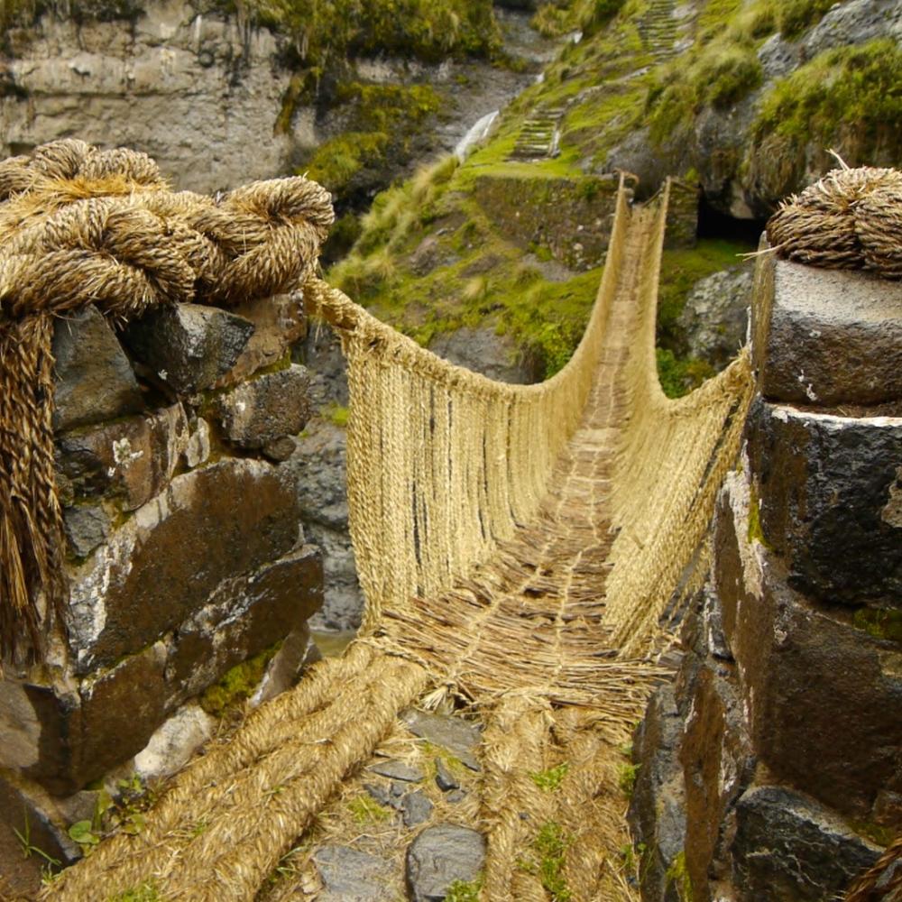 bridge made from thick, braided yellow rope, which dips down and over a chasm, with a river flowing below