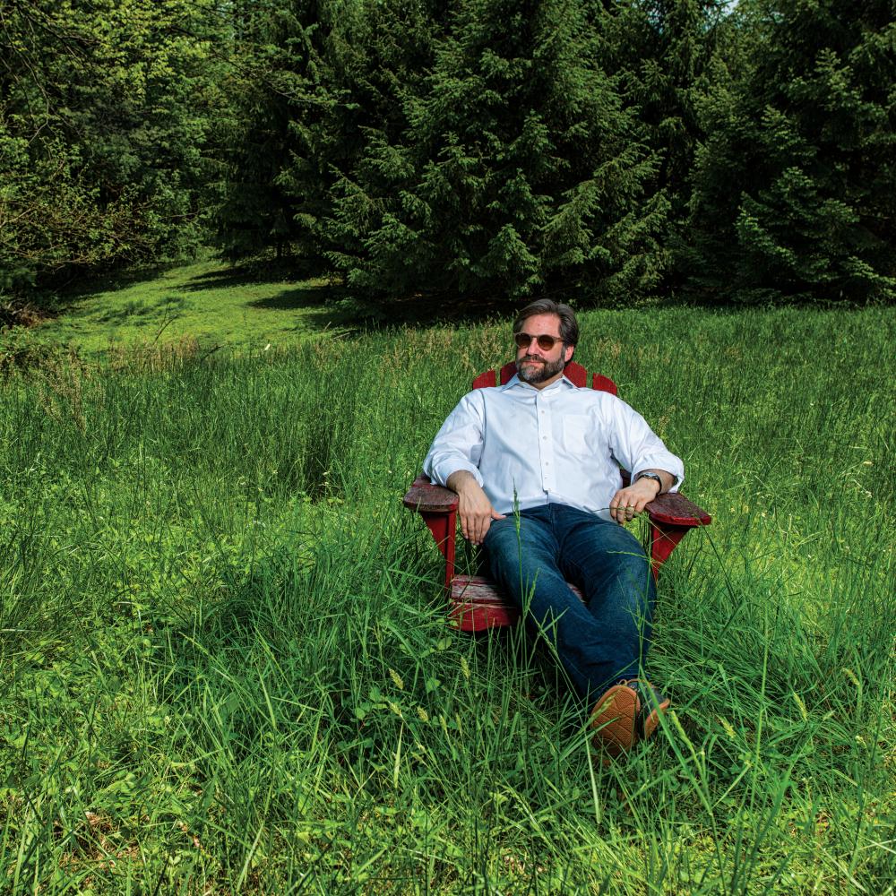 Photograph of man sitting in adirondack chair in tall grass