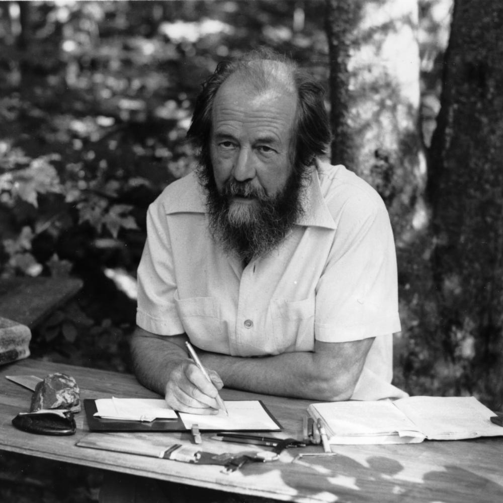 black and white photo of a bearded man writing at a table