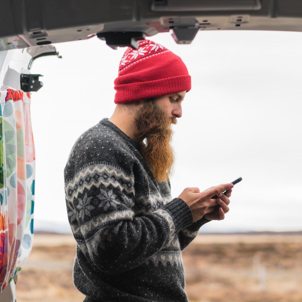 Hipster man looks at his phone in the outdoors. 