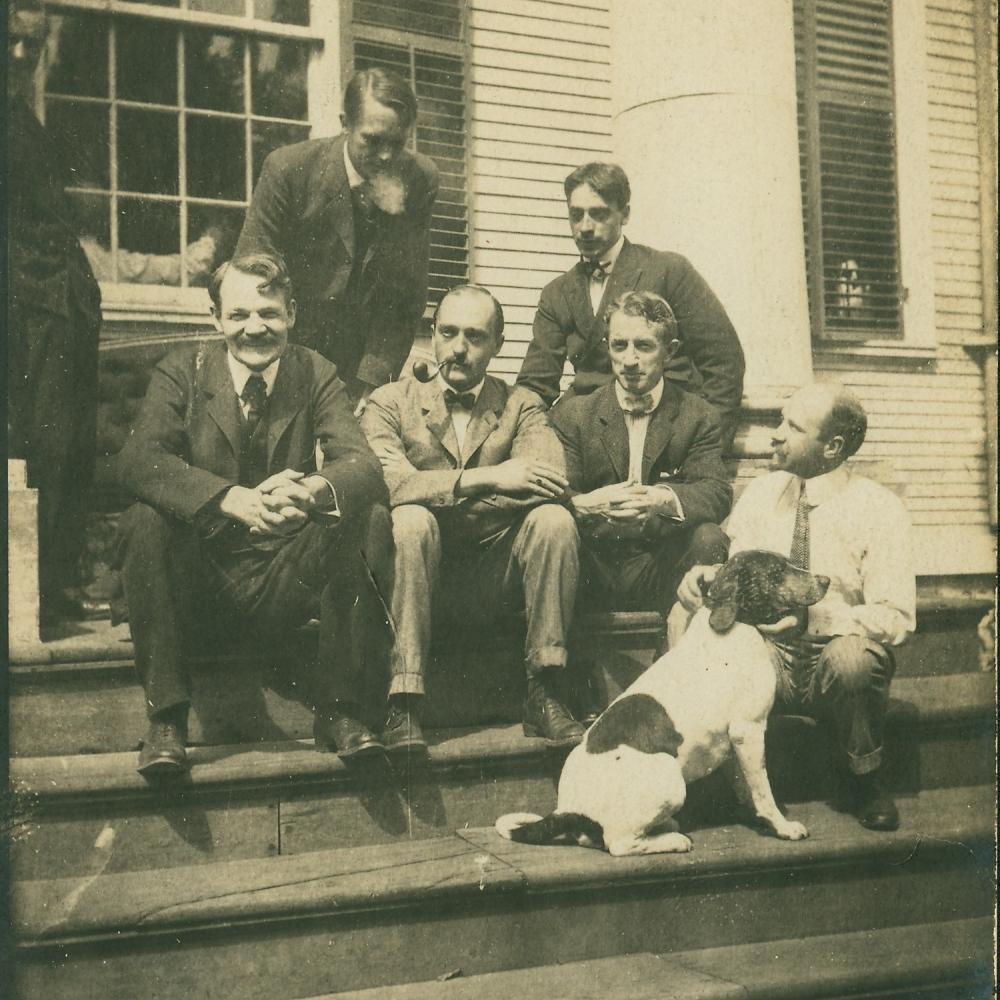 Old photo of six men and a dog sitting on steps
