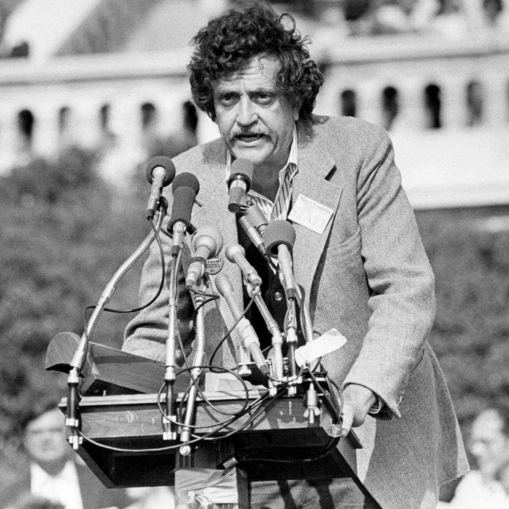 Kurt Vonnegut, speaking publicly, from behind behind a bouquet of microphones