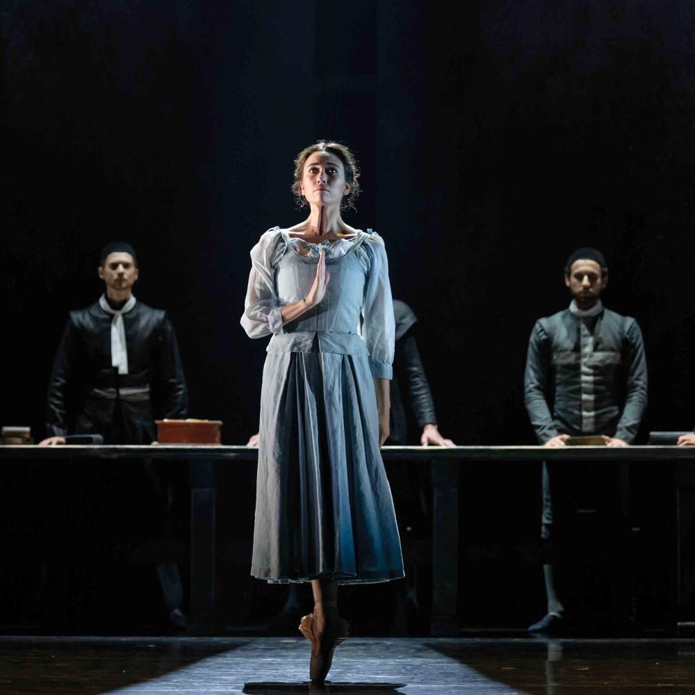 Ballet still from The Crucible, woman standing en pointe in front of 4 men.