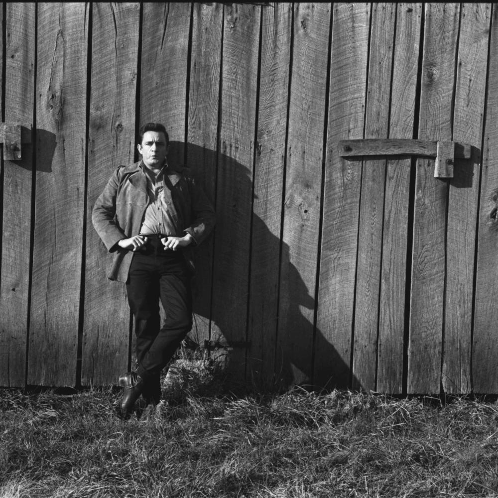Johnny Cash standing in front of wooden building.