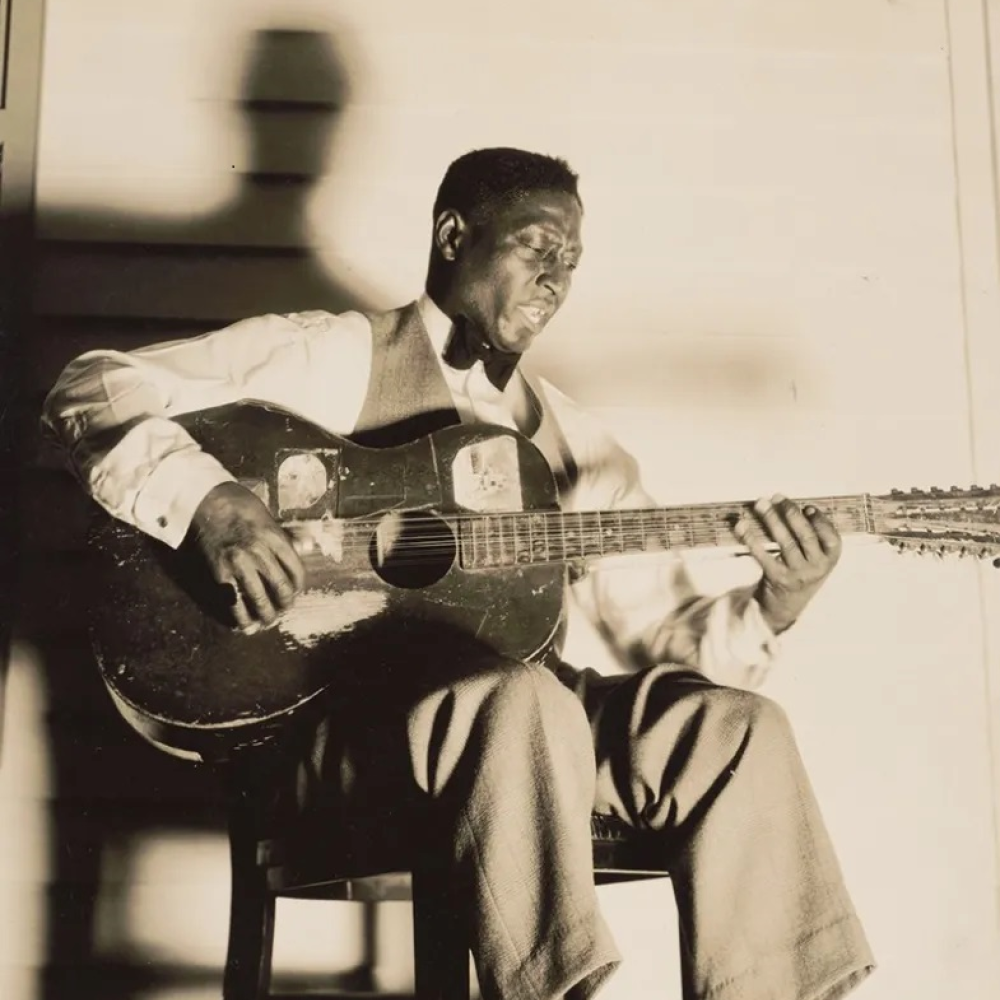 Black-and-white photo of the singer Lead Belly singing and playing the guitar. 