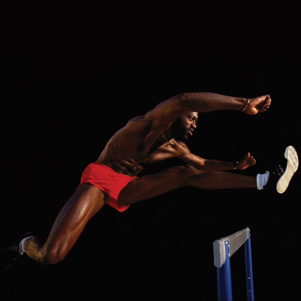 Edwin Moses leaping over hurdle against a black backdrop.