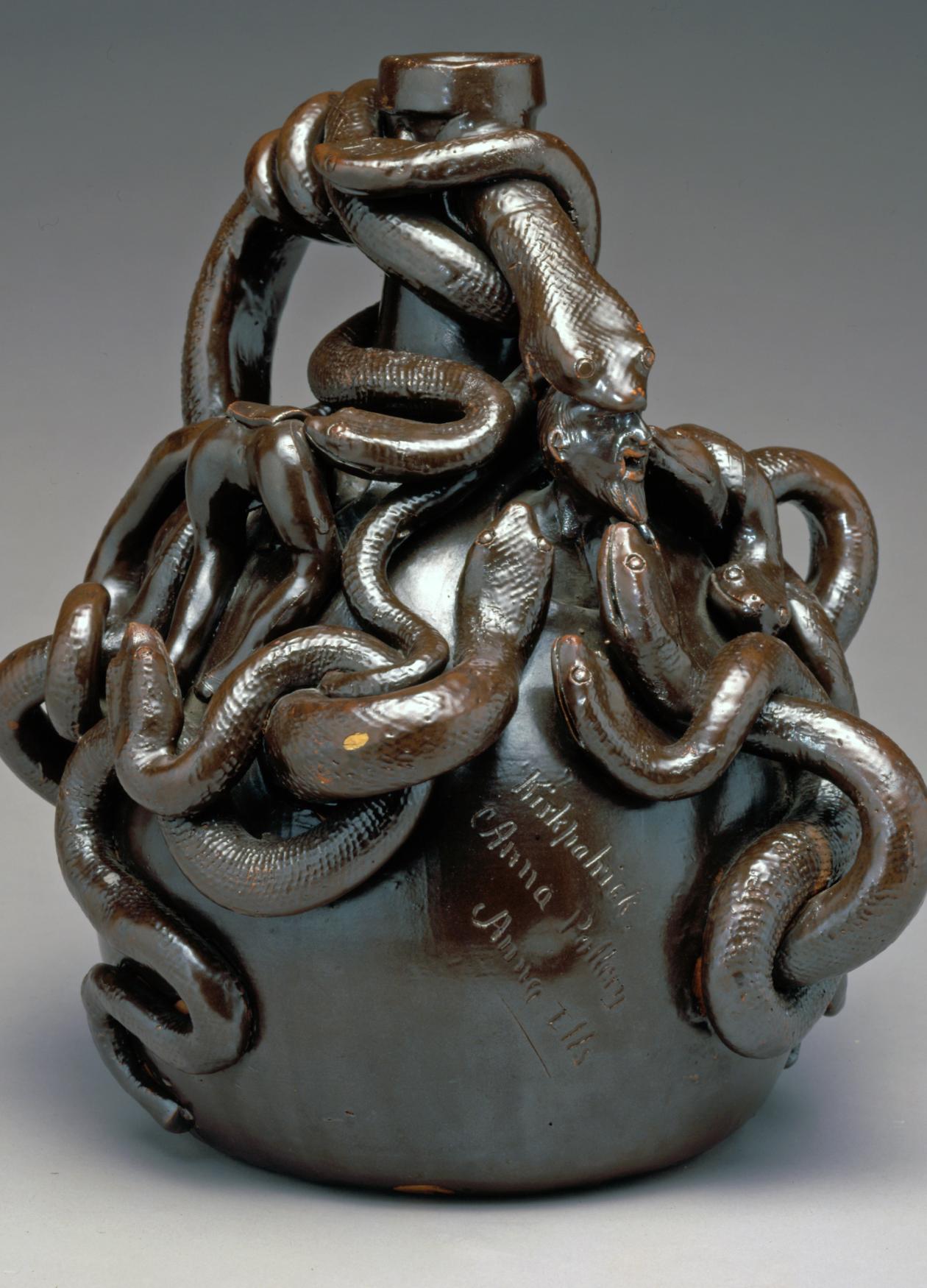 A twining mass of snakes twists around the top of a round jug with a narrow neck