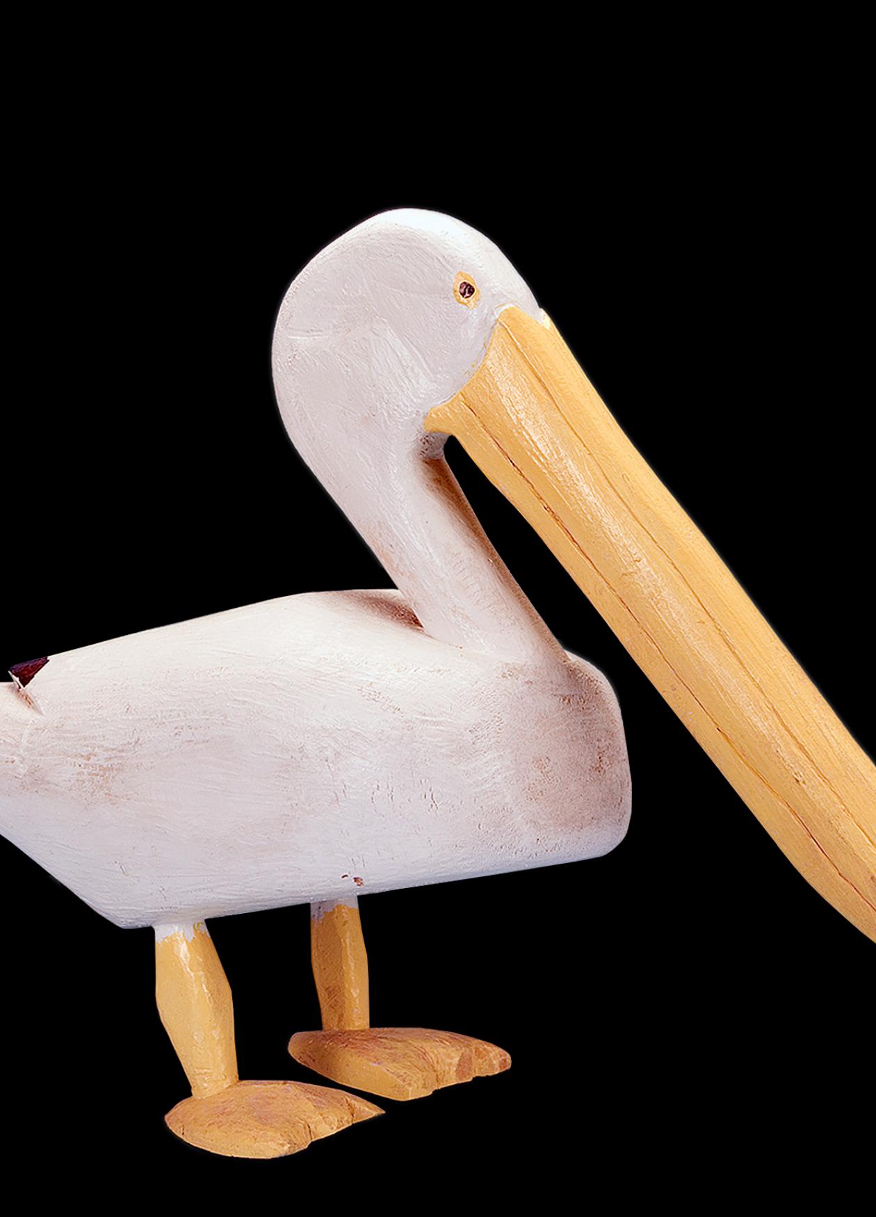 A white pelican with long yellow beak and feet, carved out of wood