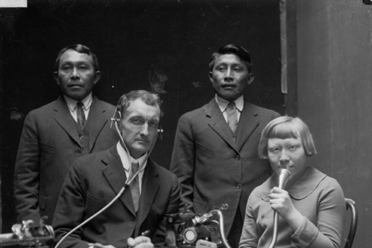 Black and white photo of men and a woman speaking into microphone
