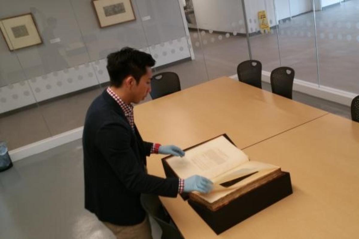 Individual with gloves on examining a large antique book