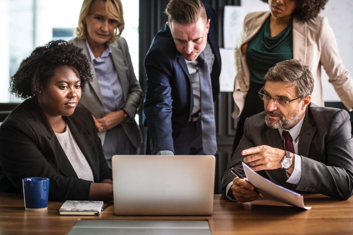 Group of people in suits meeting around a laptop