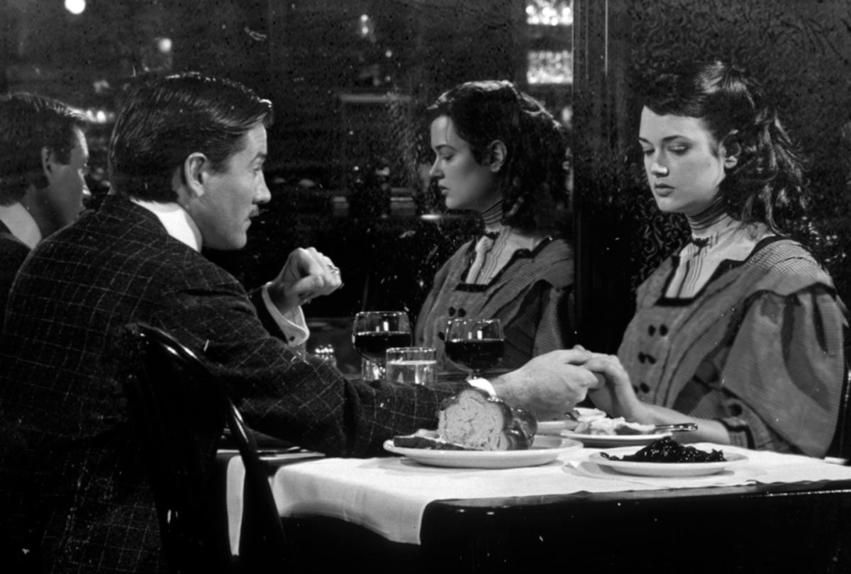 black and white film still of a man and woman holding hands across a table