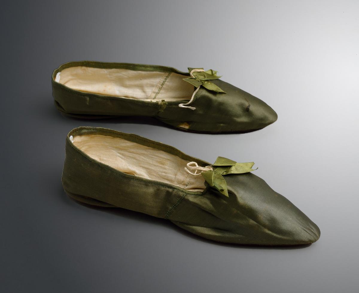 A pair of deep green satin flat shoes, with a bow on the lip