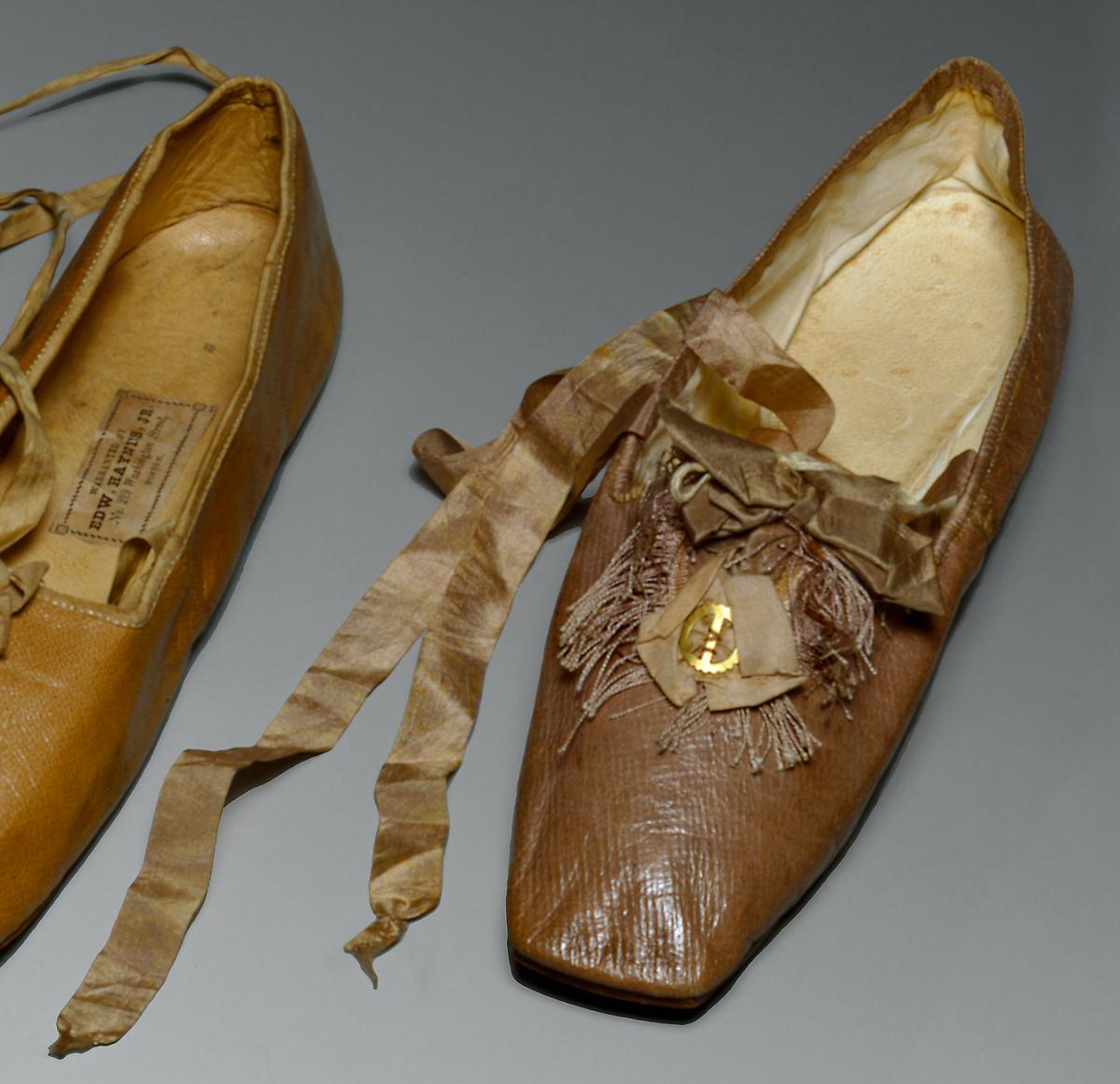 A pair of beige shoes, topped with velvet ribbon and a small charm in the shape of an anchor