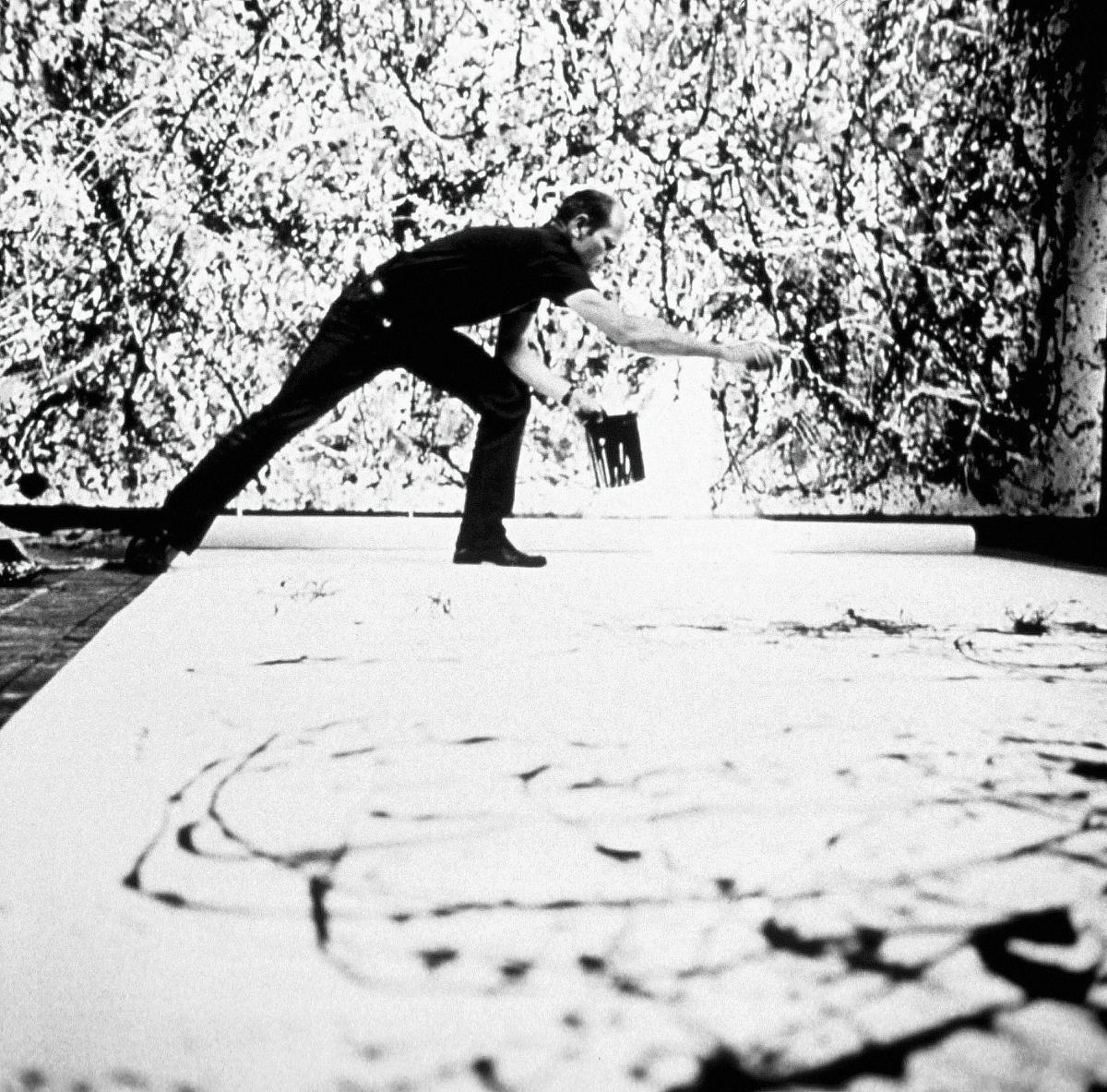 black and white photograph of a man standing over a canvas on the floor, splashing paint onto it