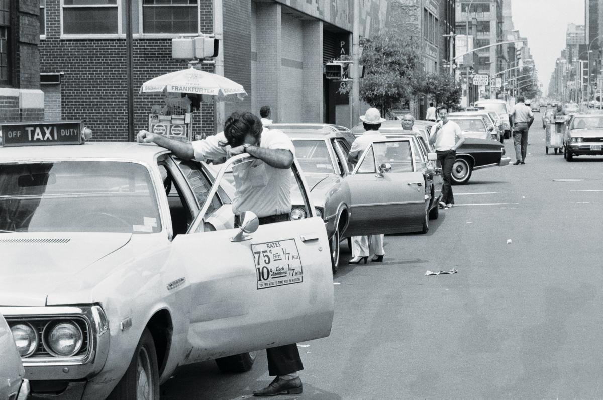 black and white photograph of people outside their cars looking frustrated